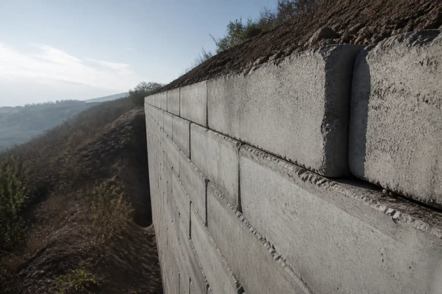 A tall retaining wall of stacked precast concrete blocks in raking light